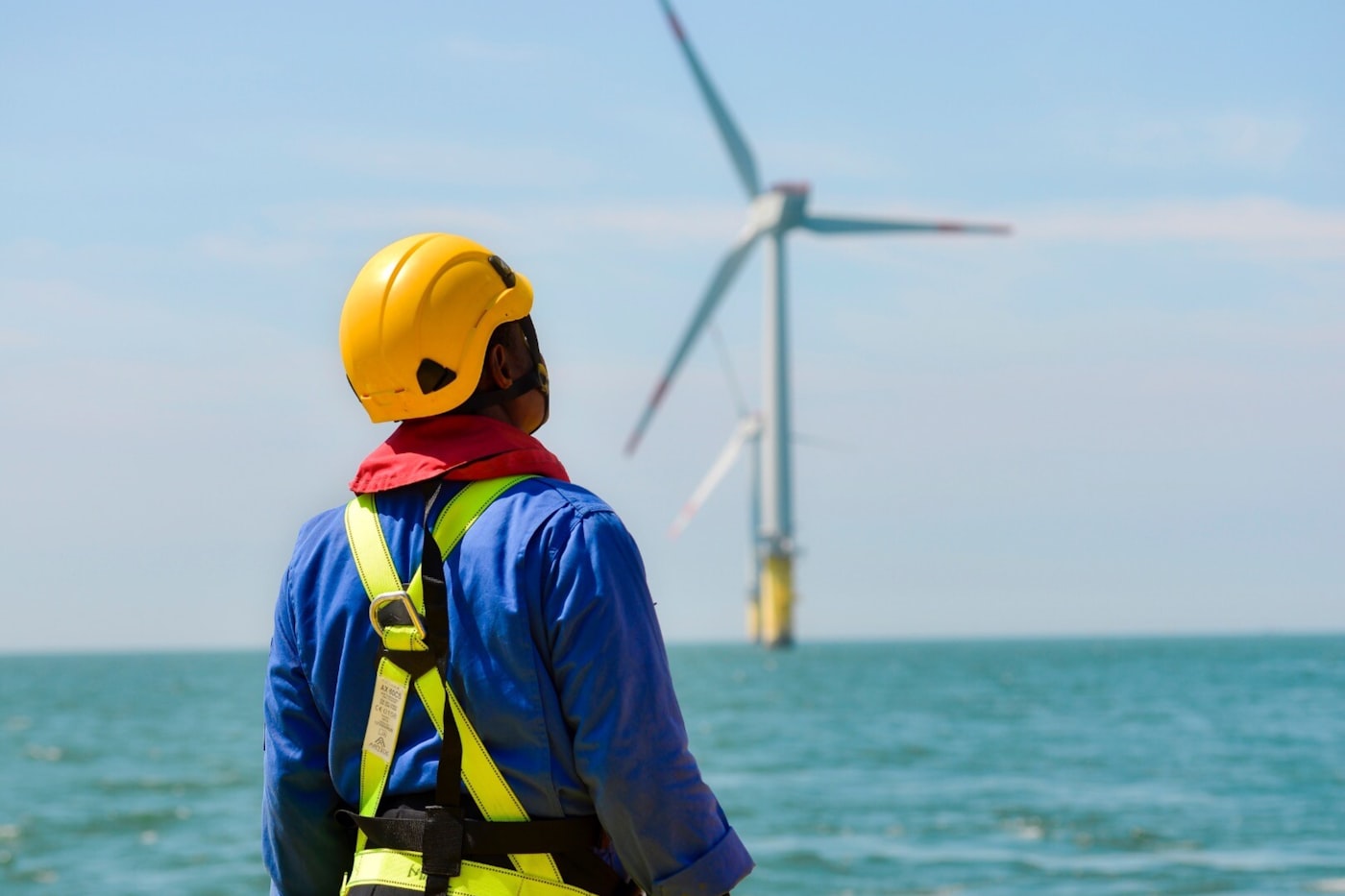 A wind turbine technician in a safety harness looking out at an offshore wind farm.
