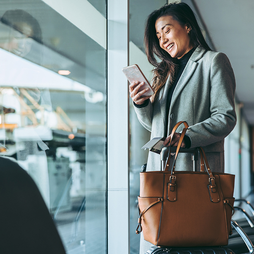 A business traveller smiles at her phone in an airport terminal.